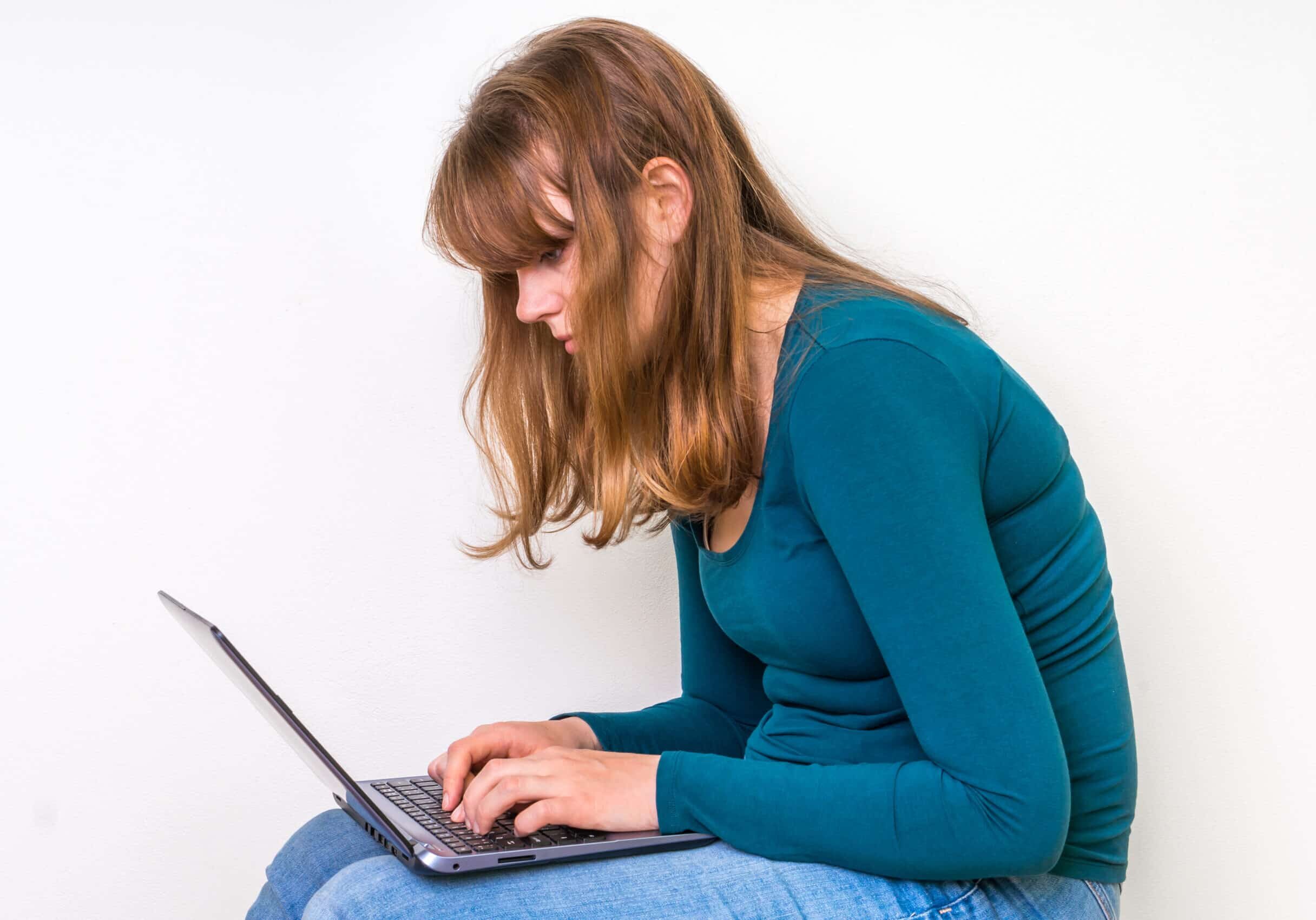 Woman is suffering from back pain sitting with laptop - concept of bad posture and bad sitting position