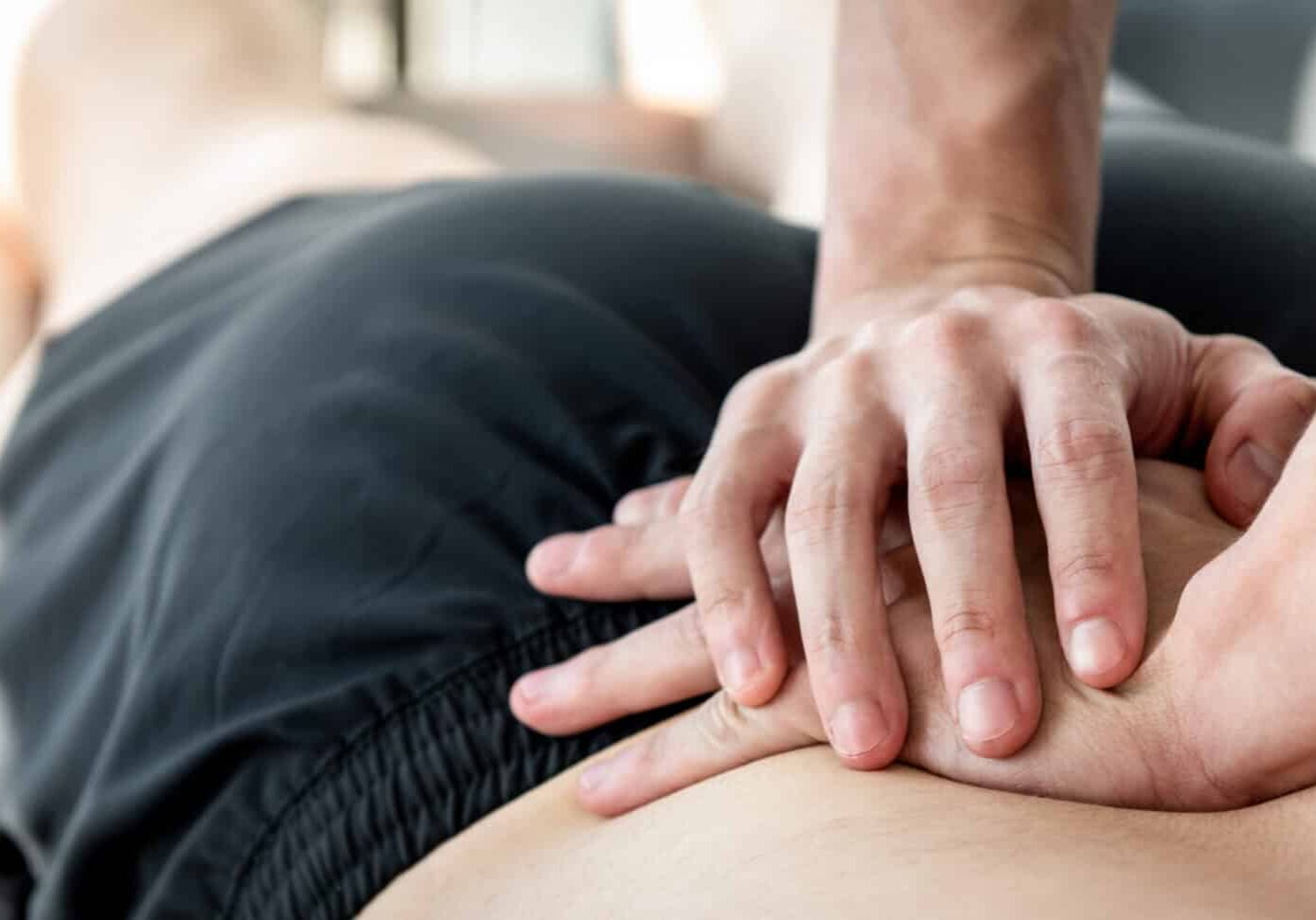 Therapist giving lower back sports massage to athlete male patient in clinic
