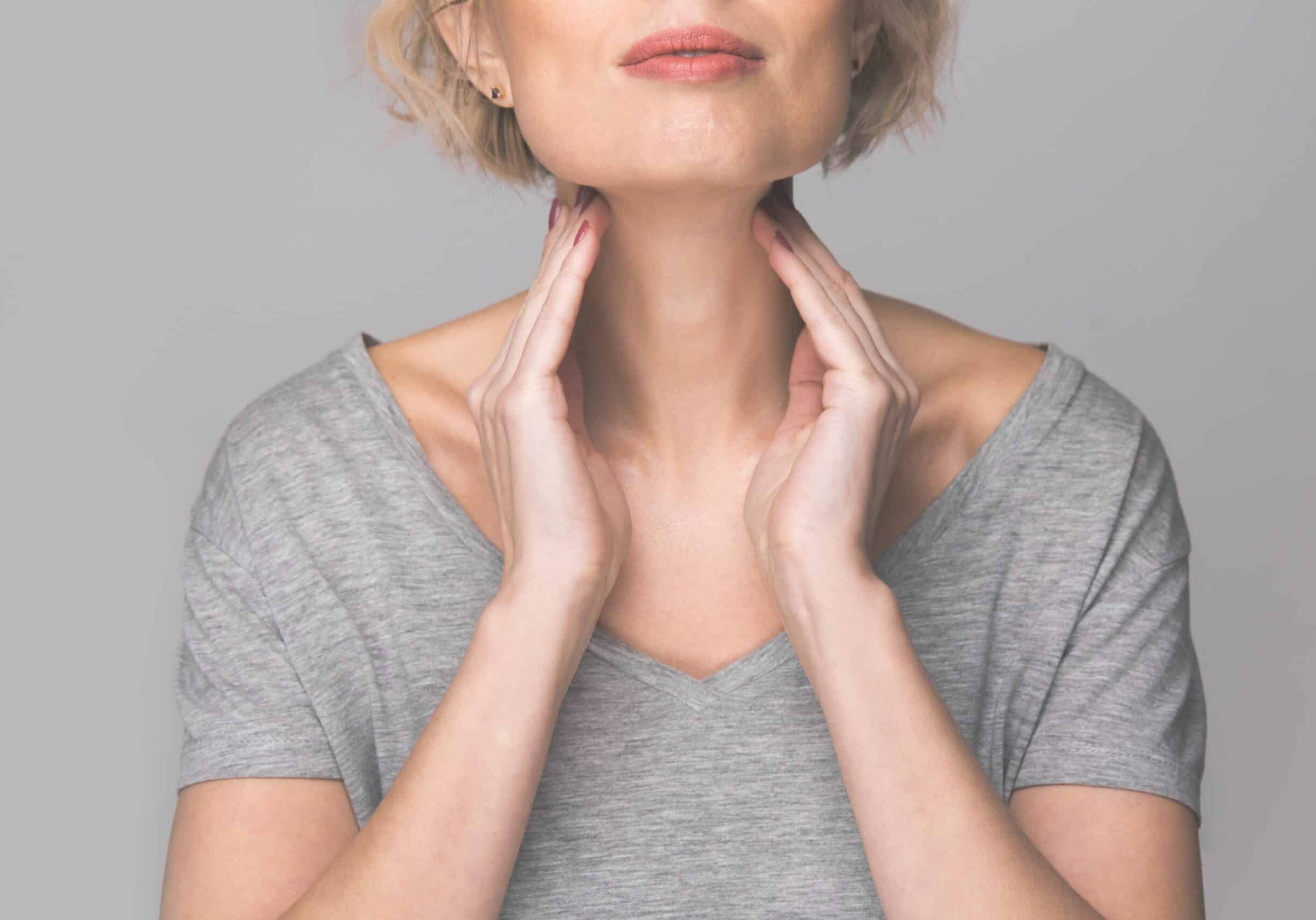Female checking thyroid gland by herself. Close up of woman in white t- shirt touching neck with red spot. Thyroid disorder includes goiter, hyperthyroid, hypothyroid, tumor or cancer Health care.