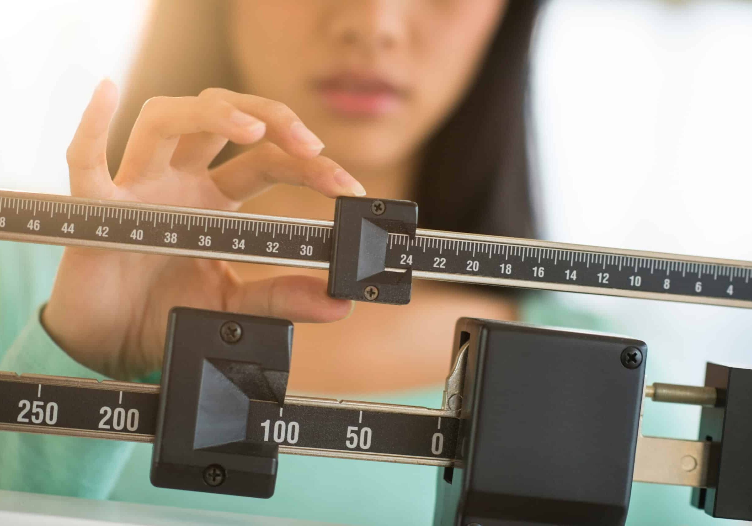 Midsection of mid adult Asian woman adjusting balance weight scale